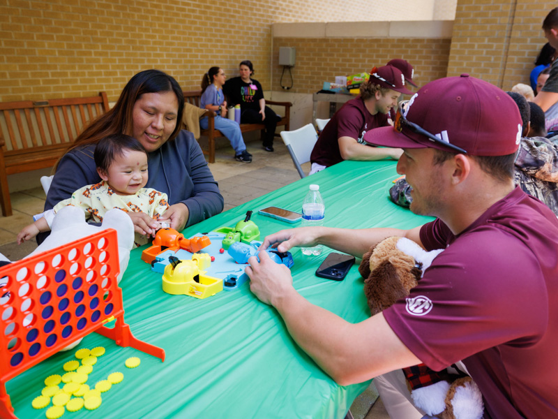 Serenity Charlie, of Philadelphia, a patient at Children's of Mississippi, enjoys some Hungry Hungry Hippos with MSU catcher Johnny Long.