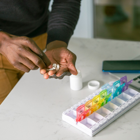 Close-up of man's hands placing prescription medication in a daily pill organizer.