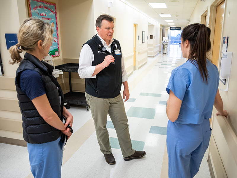Doctor in hallway talks to two residents in scrubs.