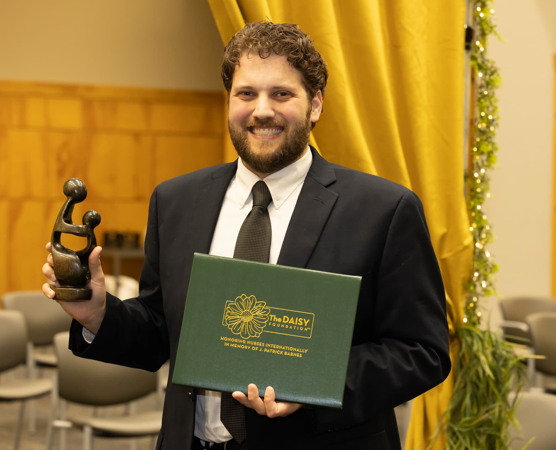 Gordon Gartrell holding trophy and green certificate holder with gold lettering: The DAISY Foundation. Honoring nurses internationally. In memory of J. Patrick Barnes.