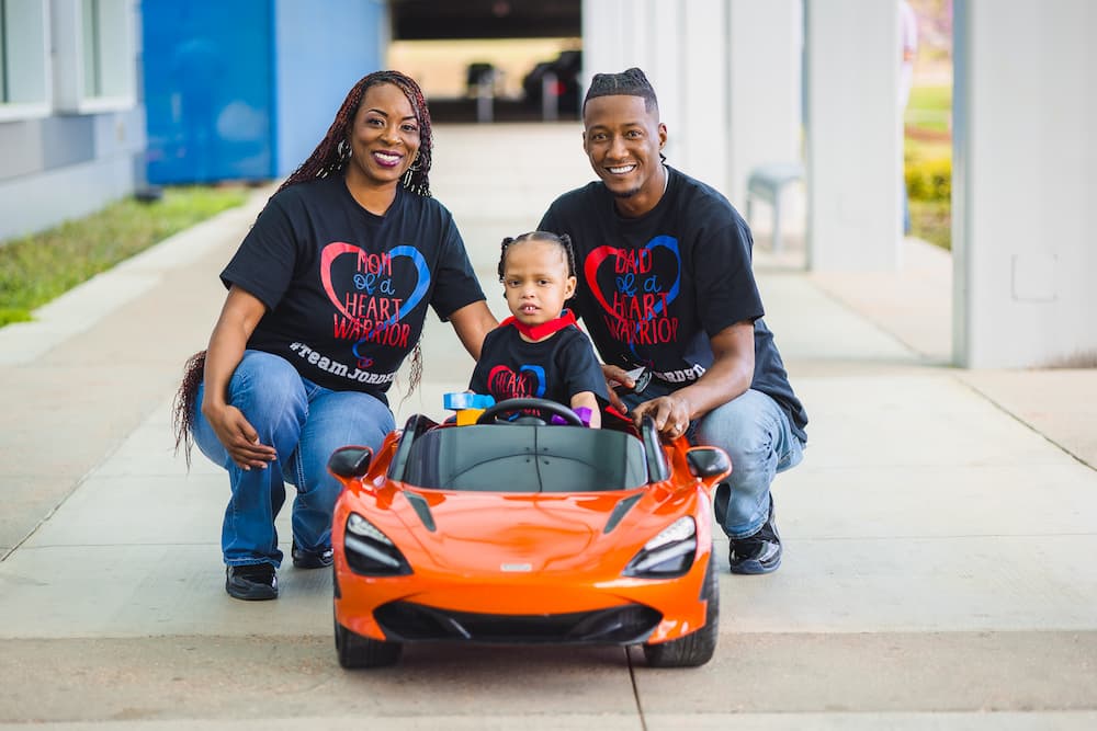 Children's Heart Center patient Jordyn Braxton and parents Jerry Braxton and Miesha Holloway-Braxton smile outside the Kathy and Joe Sanderson Tower at Children's of Mississippi.