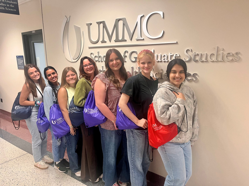 Group picture of seven Discovery U students standing outside of the School of Graduate Studies' Office with branded backpacks.