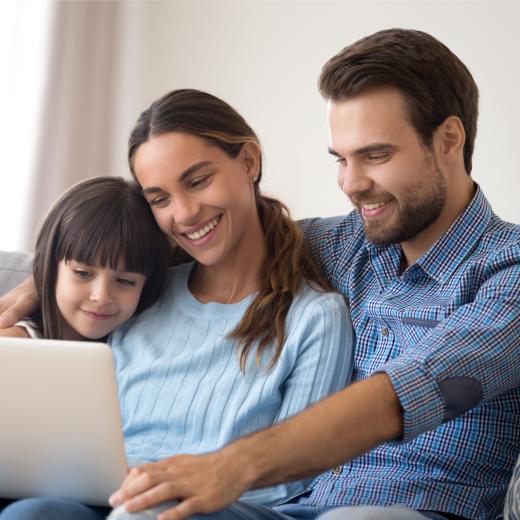 Parents hold child while looking at laptop.