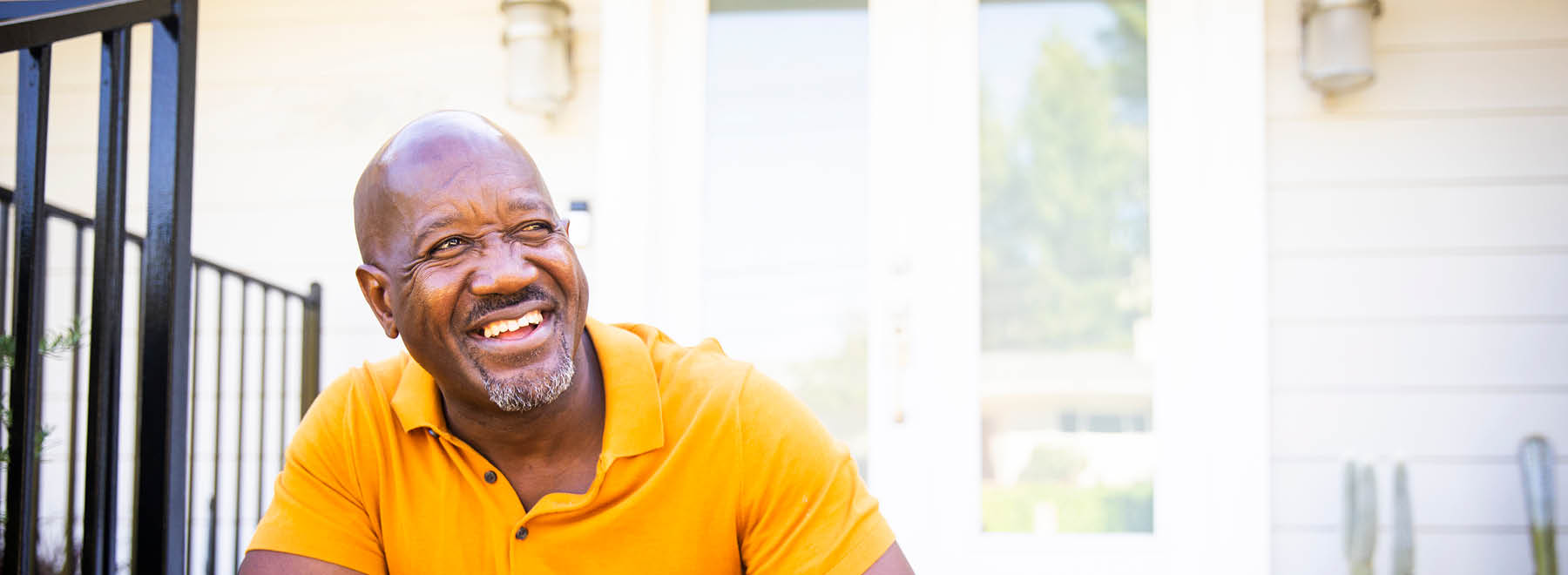 A smiling man standing sitting on a front porch step.