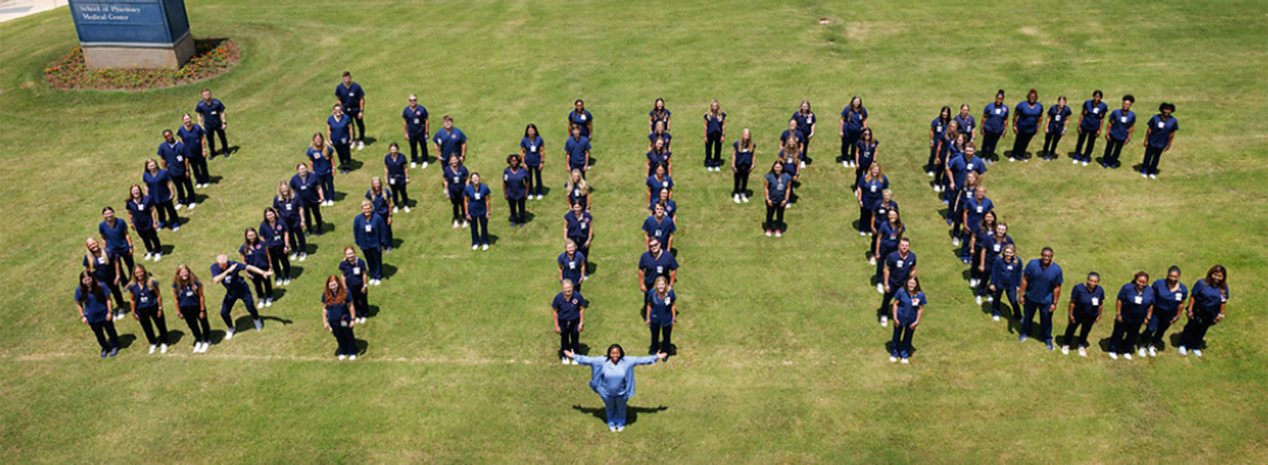An outdoor group shot of student nurse externs standing in formation to spell the letters U M M C.
