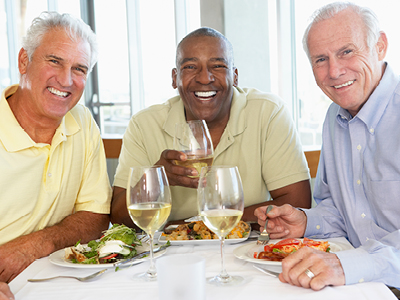 Three men seated together at a table enjoying a meal together smile for the camera.