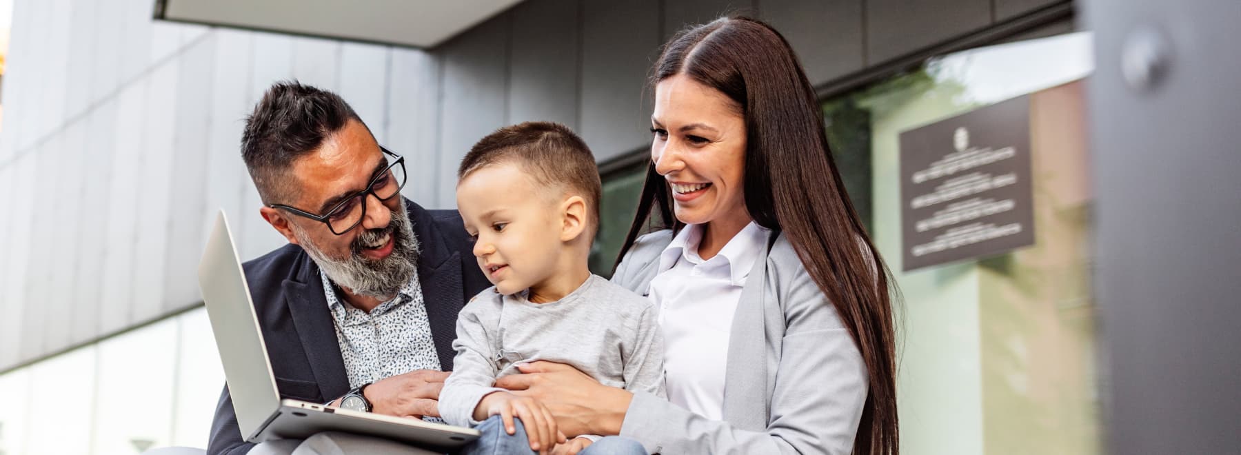 Mother, father and child smile while looking at a laptop.