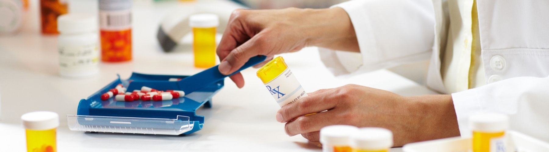 A pharmacist's hands are shown using a pill counter to fill the correct number of capsule for a prescription.