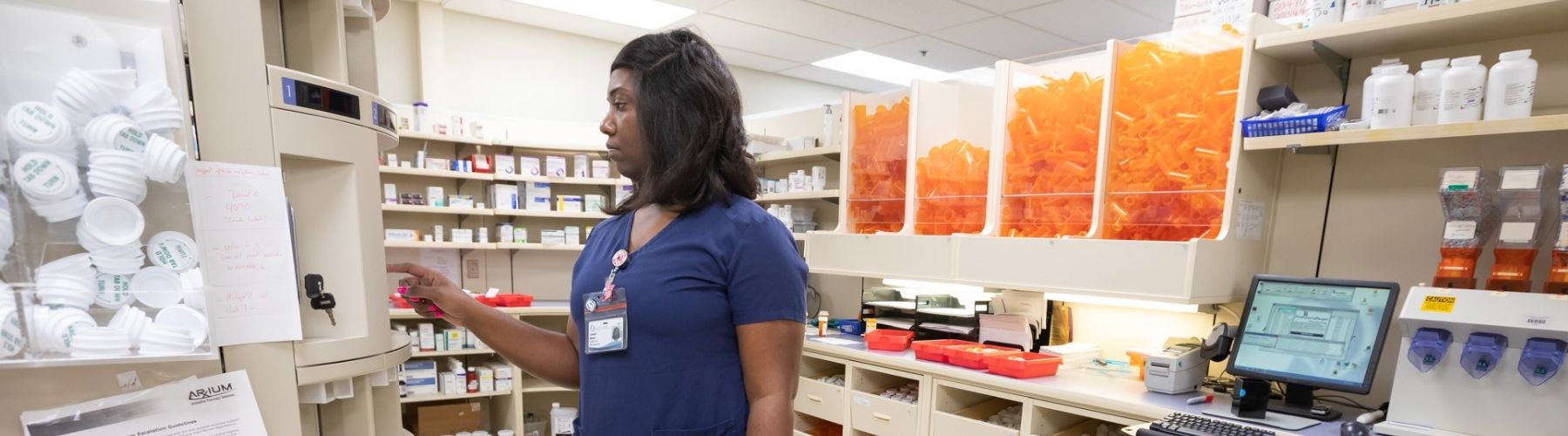 A pharmacy worker stands in the pharmacy work room performing job tasks.