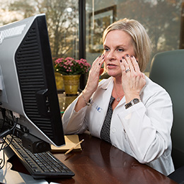 Doctor in front of laptop during telehealth session with hands on cheeks