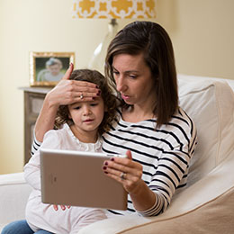 Mother feeling daughter's forehead for fever and watching laptop.