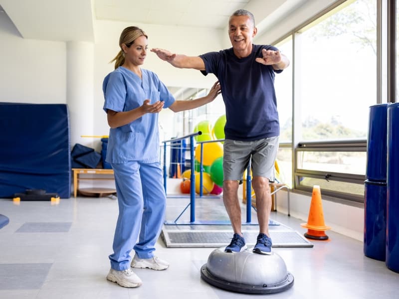 Mature man doing physical therapy exercises using a balance ball with the guidance of his therapist