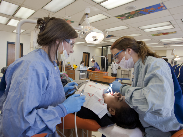 Second-year dental student, Anna Clare Saxon, left, and third-year student Kaitlyn Ellis, right, put a sealant on the teeth of Casey Elementary student Aaralyn Gray.