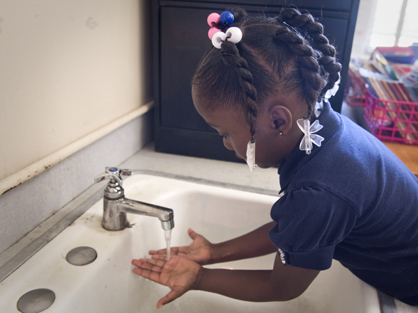 A French Elementary kindergarten student washes soap from her hands as the rest of her class sings the hand-washing song.