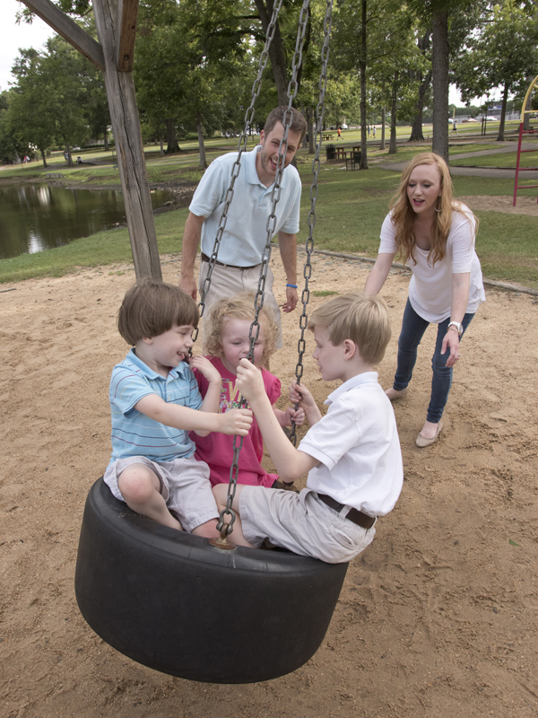 Siblings Fraiser, left, Evie Jane and Carter Johnston swing as parents Brian and Laura Beth Johnston look on.