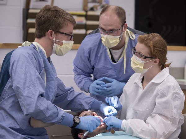 Bain, right, works in the clinic with Andrew Morgan D1, left, and Skyler Miles, D3, center. The patient is Toby Brandon, D1.