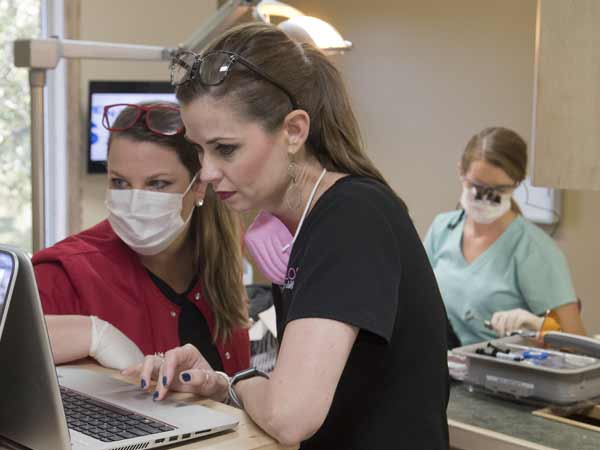 Tullos, left, and Sullivan view the patient's digital health record while Howard treats the patient in the background.