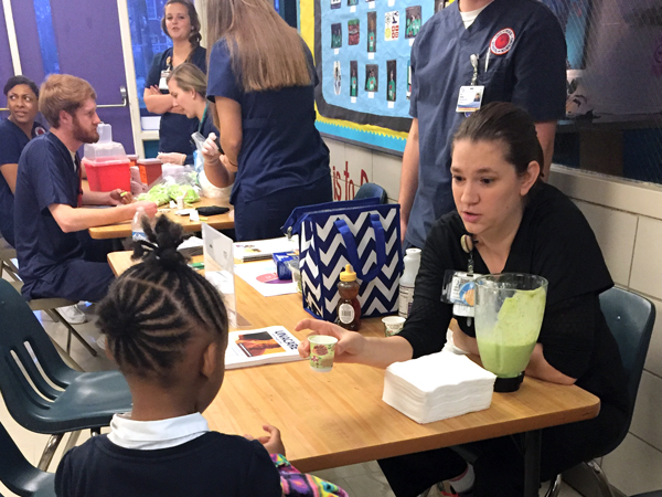 Bidwell offers a nutritious shake sample to an elementary school student at a Food Pantry Drive.