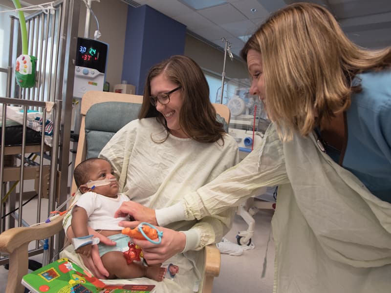 Katie McAuley, right,, an occupational therapist in Batson Children's Hospital, helps Rebecca Watson, OT2, obtain a smile from Christopher Bullock Bryant Jr., an NICU patient.