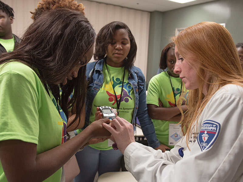 Callie Swinney, right, a fourth year pharmacy student, shows  Callaway High's Kyla Sterling how to perform a glucose test during the health fair portion of the symposium.