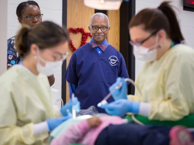 State Sen.  Hillman Frazier, center, looks on as Jolie Nguyen, left, a fourth-year dental student, and Scarlett Woods, a second-year dental student, treat Khloe Bailey, a Johnson Elementary School student. 