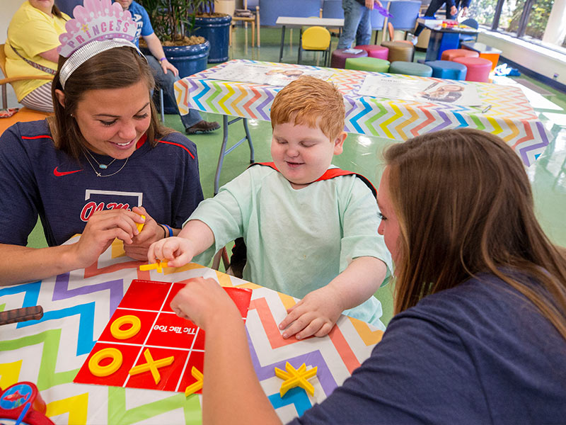 Ole Miss softball players Paige McKinney and Alyssa Clayton play tic-tac-toe with Batson Children's Hospital patient Blake Stone of Philadelphia.