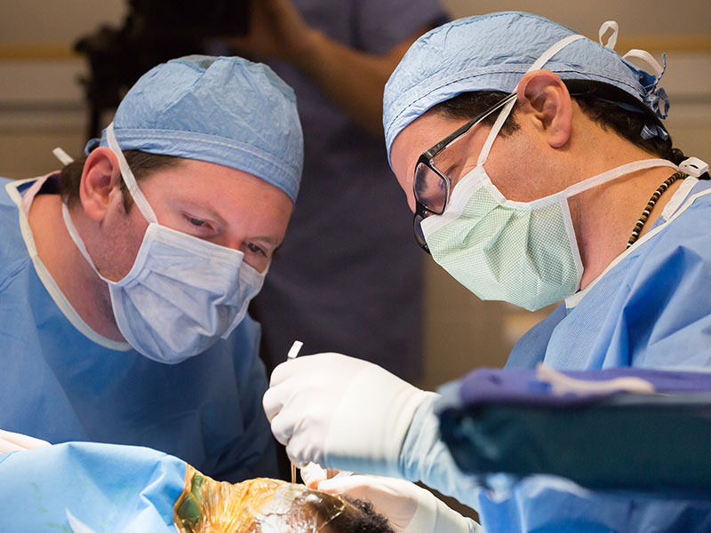 Dr. David Kowalczyck, left, fifth year otolaryngology resident, works with Dr. Jeff Carron during Kadence Lane's cochlear implant surgery.