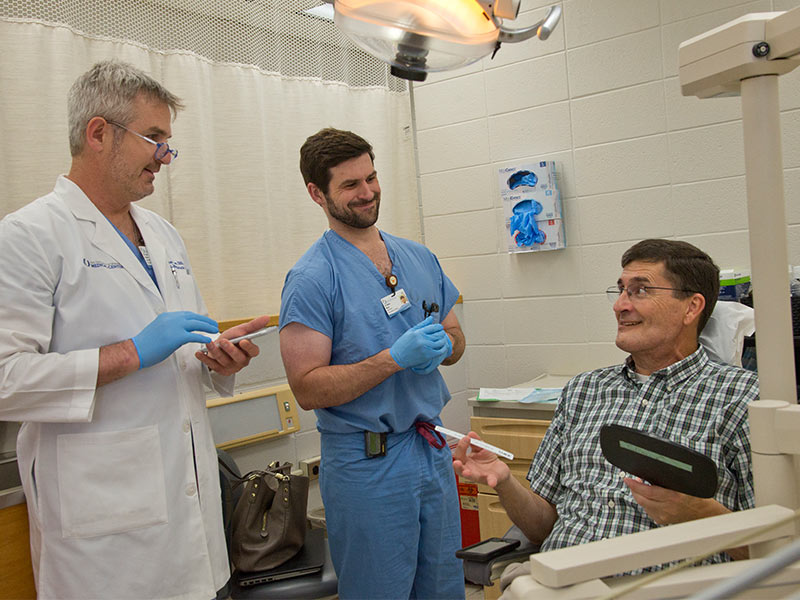 As School of Dentistry resident Walter Moses (center) assists, Dr. Ron Caloss, associate professor of oral and maxillofacial surgery, asks patient Smith to look at his teeth in a mirror shortly after Caloss clipped wires that had held Smith's jaws shut.