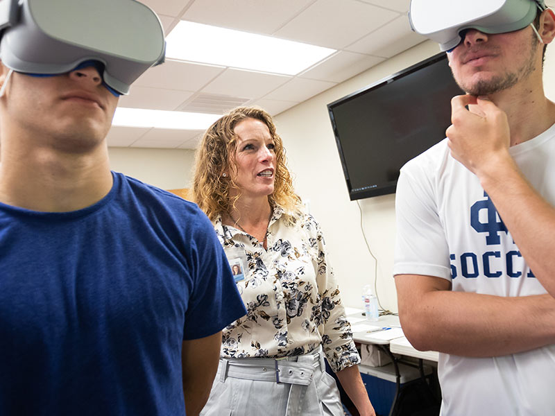Dr. Jennifer Reneker, associate professor of physical therapy, watches as soccer players Victor Bazan and Jorge Fernandez play a virtual reality game in which they track a flying fish without moving their heads.