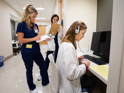 Nursing students, left to right, Molly Shotts and Laura Turner review notes while medical student Bernice Anderson has on headphones at a computer.