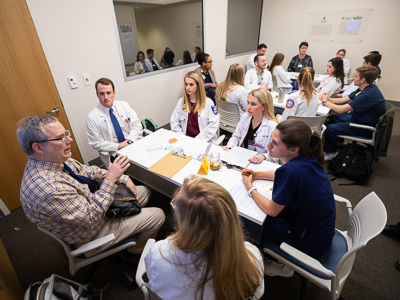 Dr. Robert Brodell debriefs two tables of students after the event.