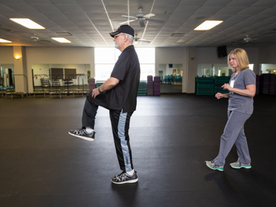 Richard Norton high-steps in an exercise to improve his balance while physical therapist Rachel Dear follows.