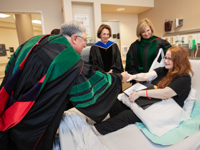 Dr. Ralph Didlake congratulates Sarah Herrington during her bedside graduation ceremony that included Dr. Jessica Bailey, Dr. LouAnn Woodward and (not pictured) Dr. Kristi Moore.