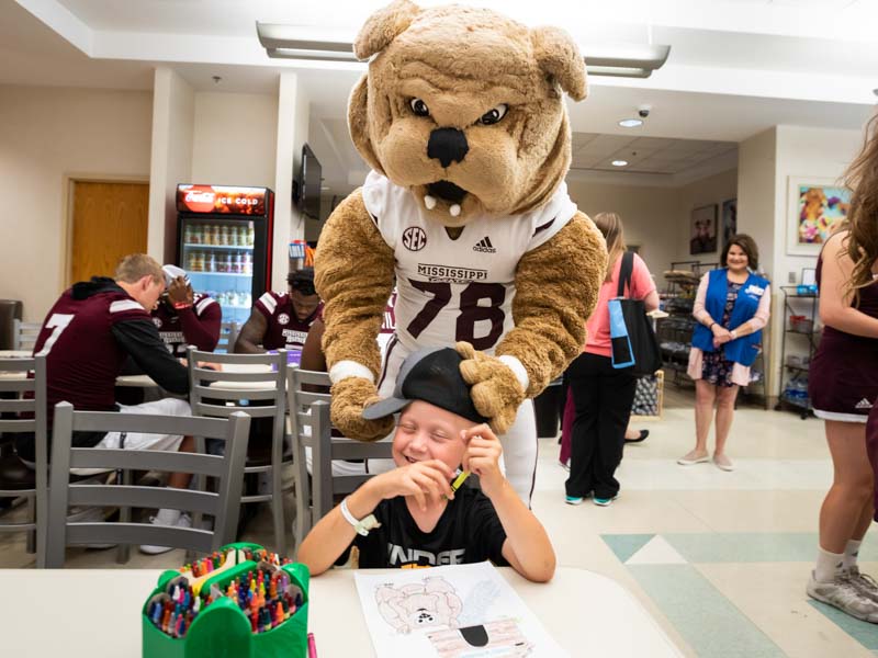 Mississippi State mascot Bully adjusts the cap of patient Lane Smith of Waynesboro.