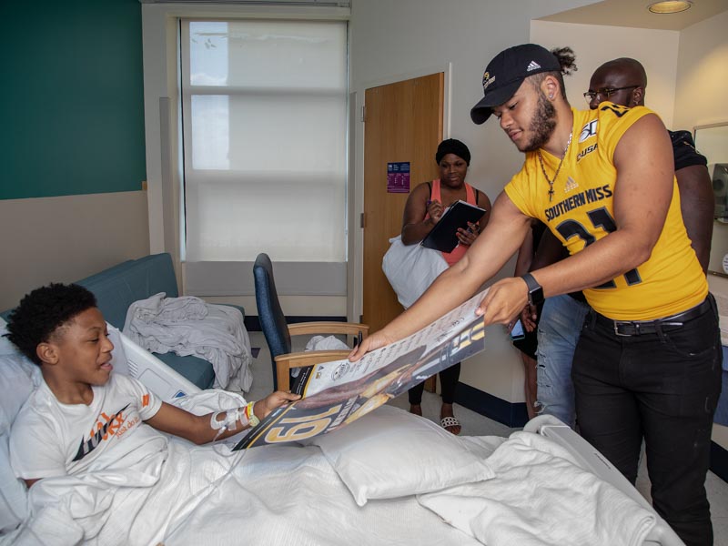 Southern Miss defensive back Rachuan Mitchell presents patient Quintarius Johnson of Bassfield with a signed Golden Eagles football poster.