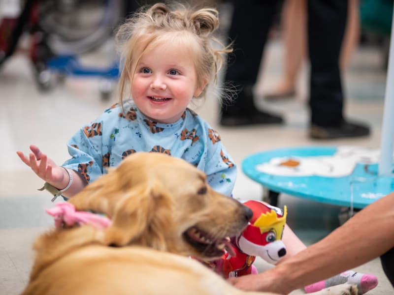 Children's of Mississippi patient Ruby Kate Greer of Hermanville smiles while visiting with Lady, a therapy dog.