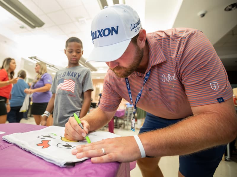 Sanderson Farms Championship golfer Zach Sucher signs one of the tournament's "chicken" bags for Children's of Mississippi patient Mason Dantzler of Pearl.
