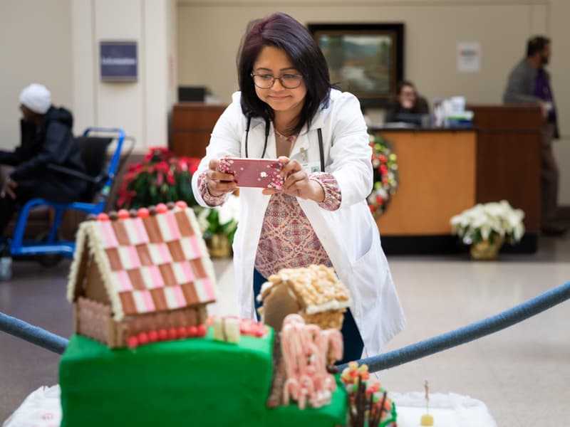 Nusrat Kabir with Internal Medicine photographs the winning gingerbread house from Pediatric Genetics.