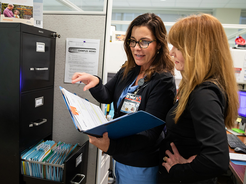 Woman opens file while another looks over her shoulder.