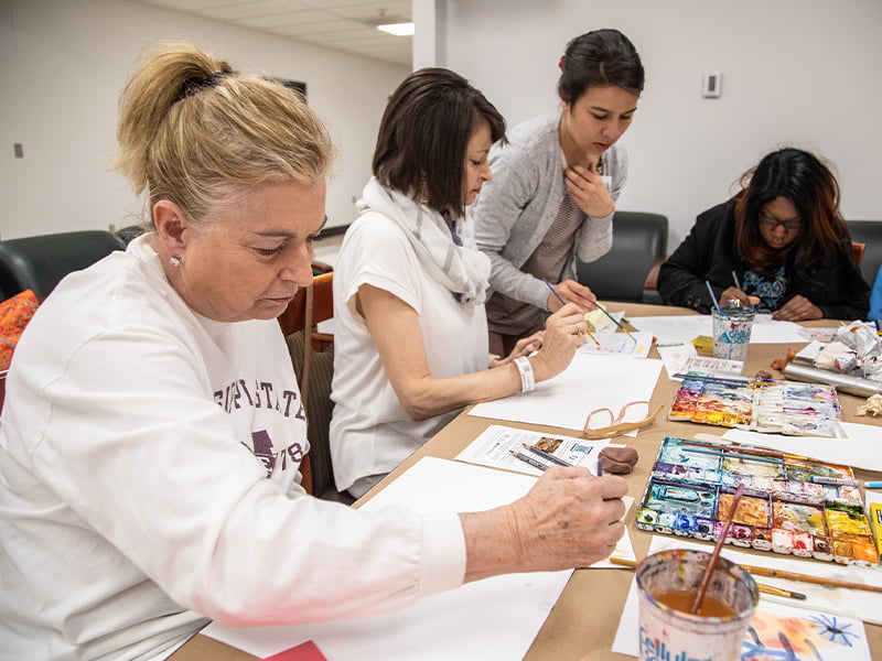 A group of four women painting at a table.