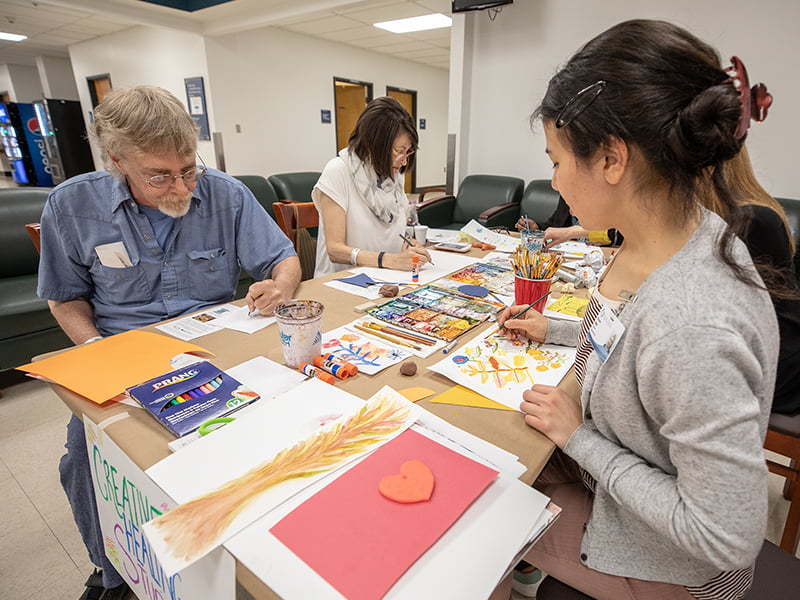 Three people painting or drawing at a table.