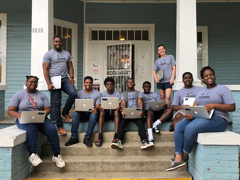 Group of people pose on porch with laptops. 