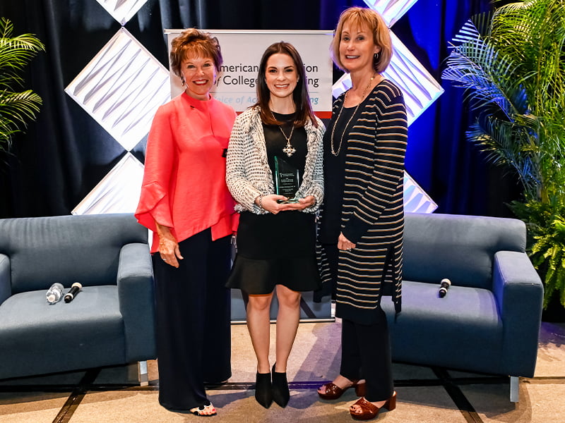 Group of three women with Katelyn Armstrong in center hold award.