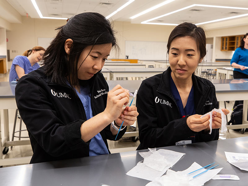 School of Medicine student volunteers, including Praise Seo, left and Aram Seo. assemble nasal swab kits in the Medical Education Building. The swabs are sterilized before use in COVID-19 testing.