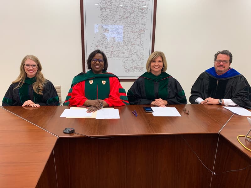 Four leaders officiating during the online Class of 2020 Commencement behind desk.