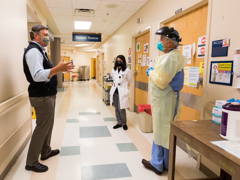 Dr. Jason Parham, left, and Dr. Bhagyashri Navalkele, center, confer with Dr. Luis Shimose Ciudad, an infectious diseases and critical care physician, before he enters a COVID-19 patient room on 2 North.