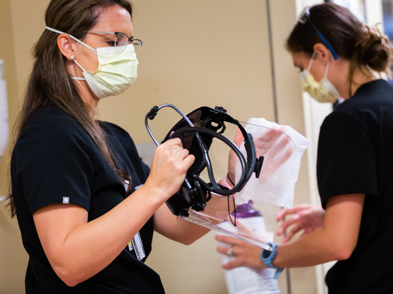 Dr. Marlee Wadsworth wipes down her face shield with disinfectant after leaving the exam room of a suspected pediatric COVID patient.