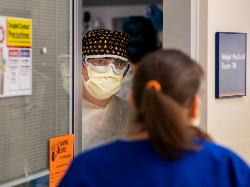 Registered nurse Jennifer Kisner quickly chats with a fellow front-line caregiver from the door of an exam room reserved for suspected or confirmed COVID patients in the Adult ED.