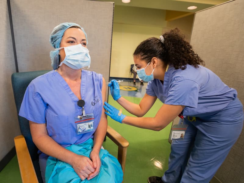 Medical student Aleysh Alejandro Ayala, right, administers a dose of the Pfizer COVID-19 vaccine to registered nurse Leslie Wilkinson.