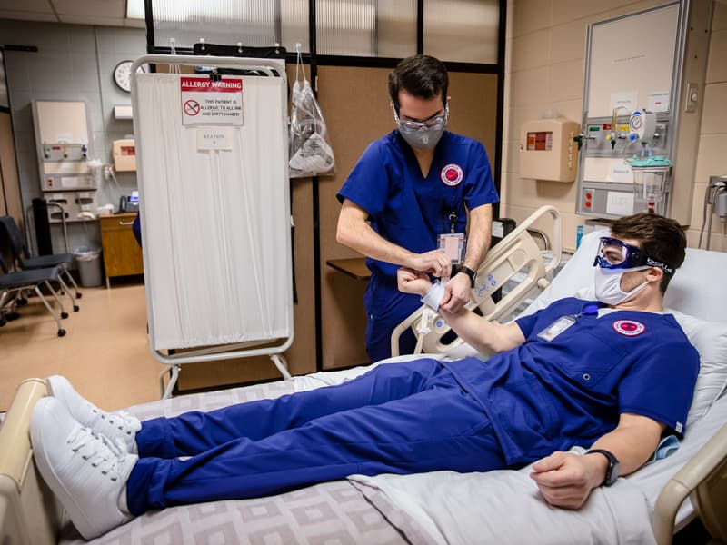 Blake McClure and Austin Oalmann practice skills in an Accelerated BSN nursing simulation lab.
